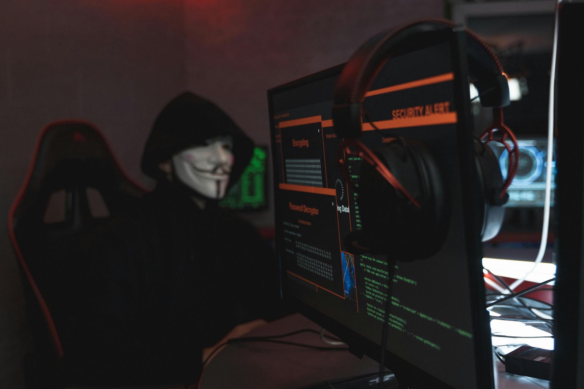 person wearing a mask sitting at a desk monitoring security systems
on a computer screen